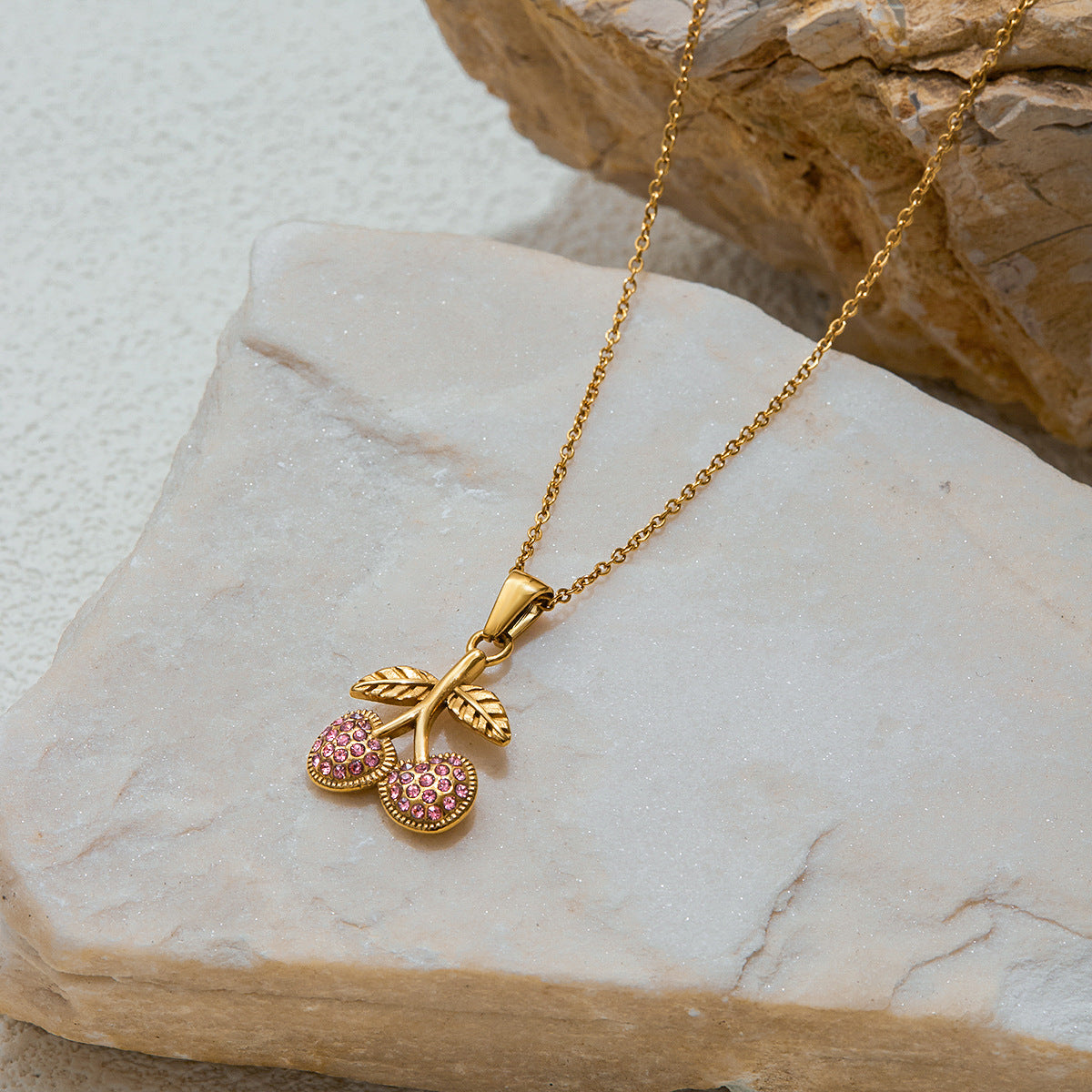 Gold necklace with a cherry pendant on a stone surface
